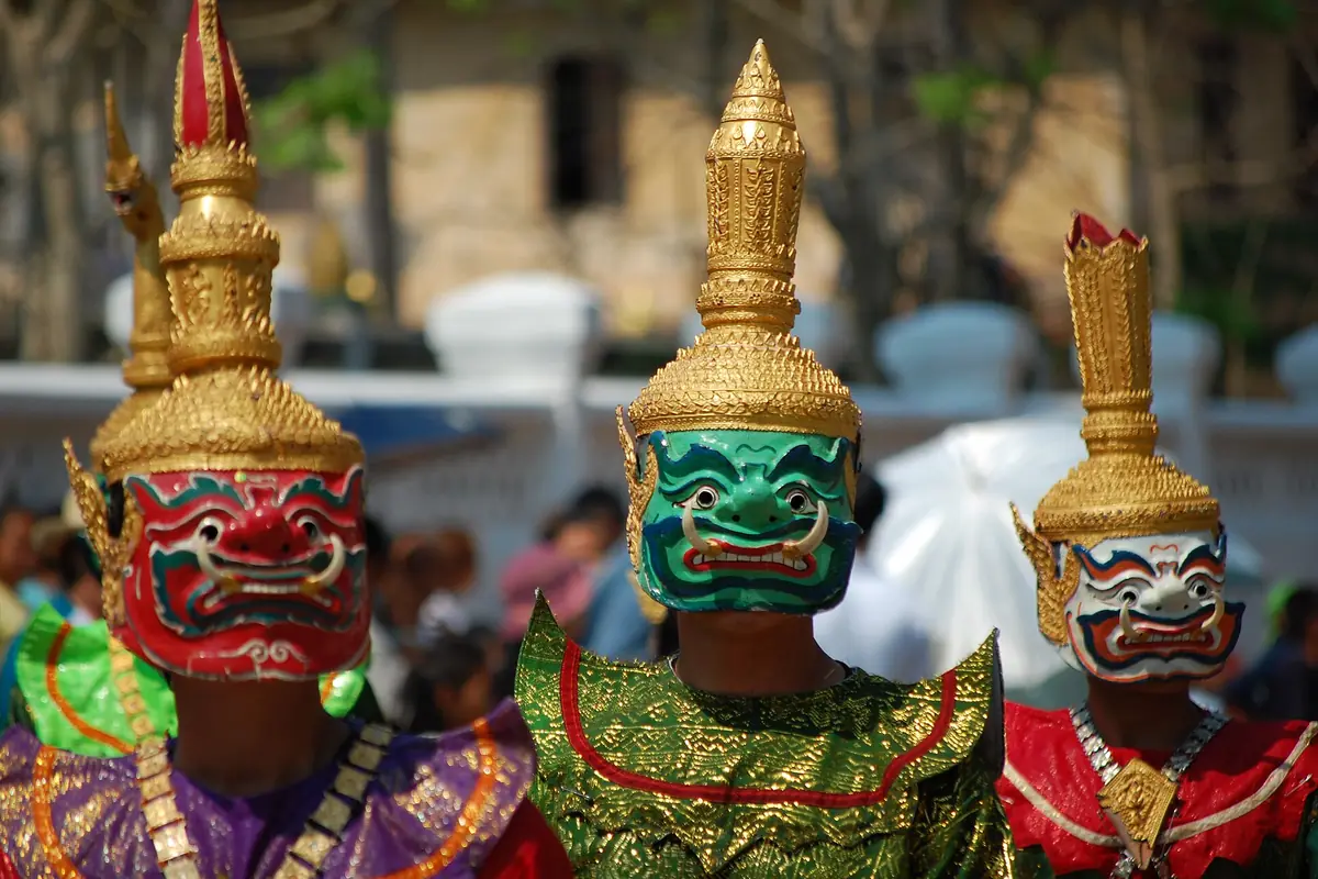 Three performers in gold crowns and painted demon masks, red, green and white, in a Lao New Year parade.